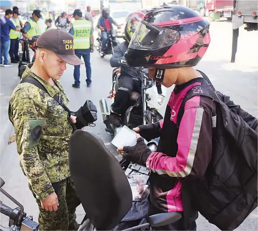  ??  ?? TIGHTENED SECURITY – A soldier inspects the papers of a motorcycle rider at a checkpoint in downtown Davao City Thursday, a day after Congress approved the extension of martial law in Mindanao. (Keith Bacongco)