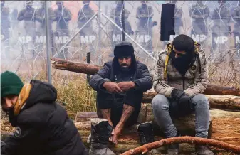  ?? Oksana Manchuk / BelTA ?? Migrants gather near Grodno, Belarus, with Polish border forces arrayed across the barbed wire fence marking the border. Thousands of migrants have been drawn to the area.