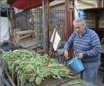  ?? PHOTOS BY CAIN BURDEAU, THE ASSOCIATED PRESS ?? Francesco Andolina splashes water on artichokes at the Ballaro market. He’s a fruit and vegetable vendor whose family has been working in the market for generation­s.