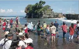  ?? Fotos: dpa ?? Ein Bild aus vergangene­n Tagen – Touristen betrachten vom Strand aus den Hindu-Tempel „Tanah Lot“, der nur bei Ebbe erreicht werden kann.