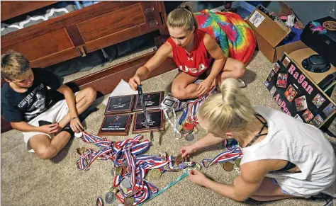  ?? LOUIS DELUCA / DALLAS MORNING NEWS ?? Gymnast Ragan Smith (center) goes through a box of medals, plaques and trophies at home in Lewisville, Texas, with the help of her brother Jackson (left) and best friend Abi Walker. Smith was the 2017 U.S. women’s gymnastics all-around champion.