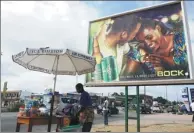  ?? ISSOUF SANOGO / AGENCE FRANCE-PRESSE ?? A vendor sells her goods next to a billboard advertisin­g Bock beer in Abidjan, Cote D’Ivoire. Bock and brewer Brassivoir­e are locked in a marketing battle.