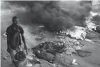  ?? ODELYN JOSEPH/AP ?? A street vendor in Port-au-prince on Friday pushes his wheelbarro­w past burning barricades set up in protest of rising fuel prices.