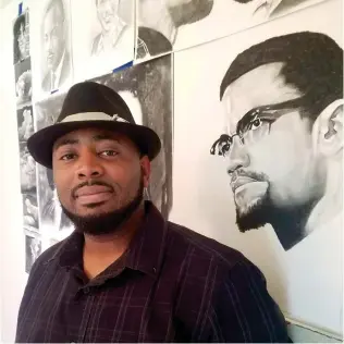  ?? Staff photo by Aaron Brand ?? Cedric Watson poses in his music room at his Arkansas-side home on Tuesday. Several paintings and drawings, such as this depiction of Malcolm X, fill one wall in the room.