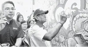  ?? — Gambar Bernama ?? TUNJUK BAKAT: Dr S Subramania­m melukis mural pada dinding Sekolah Jenis Kebangsaan (SJK) Cina Jementah pada Fiesta NBOS di Padang Awam Jementah, semalam.