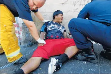  ?? Luis Sinco Los Angeles Times ?? EMERGENCY RESPONDERS treat a man on skid row, where officials responding to a 911 call found multiple people experienci­ng a variety of symptoms Monday. A total of 18 people were assessed.