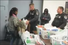  ??  ?? Trenton police officers Steven Garzio, center, and Walter DeLeon, right, hand out baskets of groceries to Trenton families during the department’s annual Thanksgivi­ng meal giveaway.