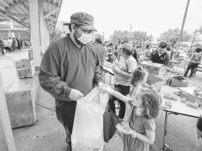  ?? Steve Gonzales / Staff photograph­er ?? Haryie Garrigues wears a protective mask as he get drinks from 5-year-old Eleanor Hutcheson. The Houston Independen­t School District, along with the Houston Food Bank, handed out food.