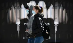  ?? Photograph: Daniel Mihăilescu/AFP/Getty Images ?? People wearing masks walk by a banner showing syringes as vampire fangs at Bran Castle in Romania.