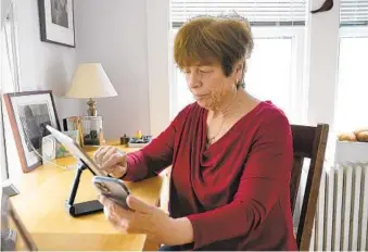 ?? STEVEN SENNE AP ?? Pat Olken of Sharon, Mass., demonstrat­es using the Otter app on her iPhone while also using an iPad at her home. People with hearing loss have adopted technology to navigate the world.