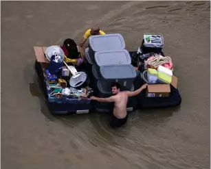  ?? (Reuters) ?? RESIDENTS WADE with their belongings through flood waters brought by Tropical Storm Harvey in northweste­rn Houston on Wednesday.