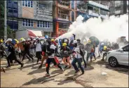  ?? (AP) ?? Anti-coup protesters run as one of them discharges a fire extinguish­er to counter the impact of tear gas fired by riot police Wednesday in Rangoon, Burma.