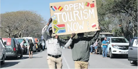  ?? ?? Two men walk down Government Boulevard lined with traffic during one of the tourism slow-drive protests.