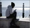  ?? ?? The Associated Press
A young man checks his phone by the Tagus river at Lisbon’s Comercio square on a sunny winter day.