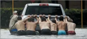  ??  ?? People push a stalled pickup through a flooded street in Houston after Tropical Storm Harvey dumped heavy rains Sunday.