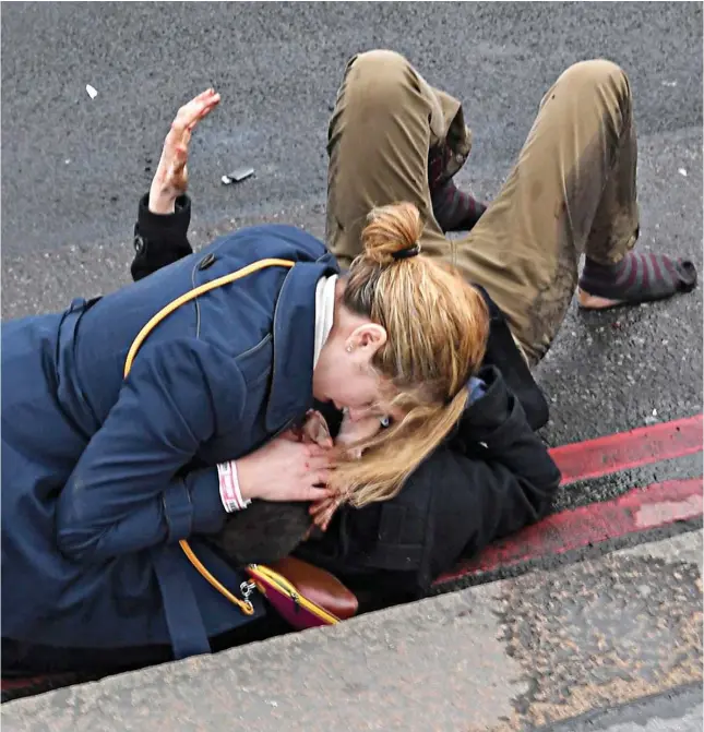  ??  ?? Good Samaritan: One of the victims holds a bloodied hand in the air as a woman cradles his head on Westminste­r Bridge yesterday