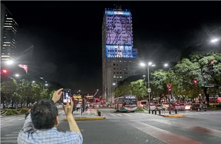  ?? AP ?? Supporters take an image of the iron portrait of the late Eva Peron at the building now hosting the ministries of social developmen­t and health as it becomes illuminate­d after four years in darkness in Buenos Aires.