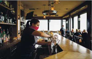  ?? PHOTOS BY CELESTE NOCHE — THE NEW YORK TIMES ?? A bartender pours cocktails at Pickled Fish, a restaurant located at the Adrift Hotel in Long Beach, Washington. The restaurant has reopened with socially distanced seating and mask-wearing servers.