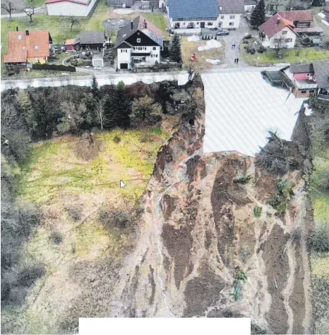  ?? FOTO: FEUERWEHR ?? Ein Drohnenfot­o zeigt das Ausmaß des Erdrutsche­s im Wangener Weiler Rhein kurz nach dem Unglück noch ohne Schnee. Das am stärksten betroffene Haus rechts oben bleibt bis auf Weiteres geräumt. Die Abrisskant­e an einer Straße wurde zum Schutz vor Regen mit einer Plane abgedeckt.