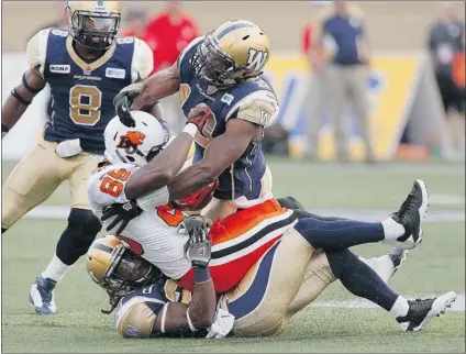  ?? JOHN WOODS/ CANADIAN PRESS ?? B. C. Lions’ receiver Shawn Gore is sandwiched by the Winnipeg Blue Bombers’ Alex Suber ( bottom) and Henoc Muamba ( right) during the first half of their game in Winnipeg on Friday. Neither offence had much room to manoeuvre during the CFL contest,...