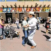  ??  ?? Fiesta-goers dance during Fiesta in 2010. In the background is the Palace of the Governors, decorated with plaques bearing Spanish coats of arms of local families’ ancestors.