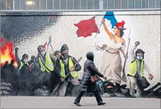  ??  ?? A woman in Paris passes by a mural depicting yellow vest (gilets jaunes) protesters inspired by a painting by famous French artist Eugene Delacroix