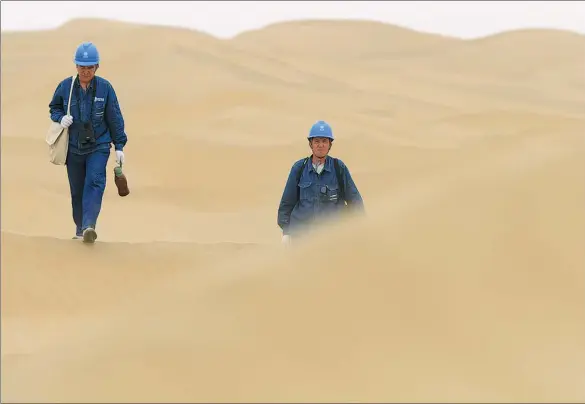  ??  ?? Ahmat Tohti (right) and a colleague walk toward a power tower in the Taklimakan Desert during a regular inspection.