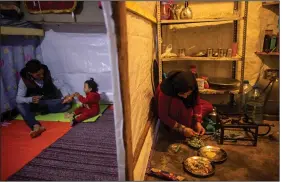  ?? (AP/Hassan Ammar) ?? Syrian refugee Ayesha al-Abed, 21, (right) prepares food as her husband, Raed Mattar, 24, (left) plays with their daughter Rayan before they break their fast April 13, first day of the fasting month of Ramadan, in a refugee camp in Tripoli, Lebanon.