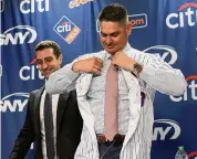  ?? Bebeto Matthews/Associated Press ?? New York Mets new manager Carlos Mendoza puts on a Mets jersey during a press conference in New York on Tuesday. At rear left is Mets president of baseball operations David Stearns.