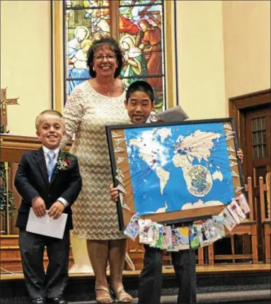  ?? PHOTOS PROVIDED ?? Members of the graduating sixth-grade class at Sacred Heart School present a gift to retiring school Principal Susan Merrill during their commenceme­nt on Thursday. The map details Merrill’s future travels during her retirement.