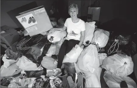  ?? Arkansas Democrat-Gazette/THOMAS METTHE ?? Karla Allen, who with her husband and son founded Ozark Water Projects, sits atop a pile of donated shoes in her garage. The shoes will be sold by the pound to exporters and distribute­d throughout the world, while proceeds from the shoes will fund the...