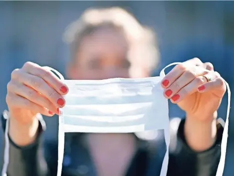  ?? FOTO: MICHAEL WEBER/IMAGO ?? Eine Frau legt an der frischen Luft ihre Mundschutz­maske an.