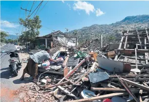  ?? ADEK BERRY/AFP/GETTY IMAGES ?? A villager tries to salvage belongings from the ruins of a house in Pemenang, Lombok. Rescuers were battling collapsed bridges, blackouts as well as damaged roads blocked with debris.