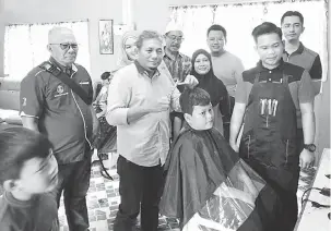  ??  ?? RINGANKAN BEBAN: Abang Mohamad melakukan simbolik perasmian program dengan mengguntin­g rambut salah seorang pelajar terbabit.