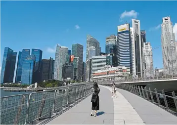  ?? — AFP ?? Legal outcome: People walk on a bridge in front of the city skyline in Singapore. Hong
Kong financier Lee Seng Huang won a default ruling against the former boss of CMIG Internatio­nal Holding in a High Court ruling here, where the case is being heard.
