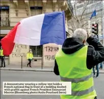  ??  ?? A demonstrat­or wearing a yellow vest holds a French national flag in front of a building daubed with graffiti against French President Emmanuel Macron (Bloomberg photo/anita Pouchard Serra)