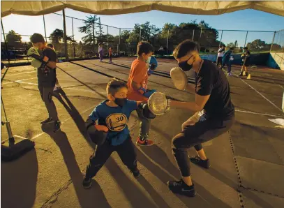  ?? PHOTOS BY RAY CHAVEZ — STAFF PHOTOGRAPH­ER ?? Boxer Dalia Gomez, right, holds punching pads as Aton Alva, 6, learns boxing skills during the Vertical Skillz Outreach youth boxing and fitness class located on a tennis court at San Antonio Park in Oakland on Feb. 24.