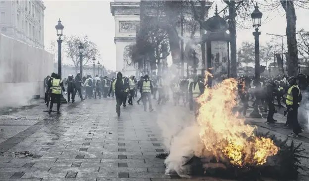  ??  ?? 0 Protesters wearing yellow vests stand next to a burning tree, as they demonstrat­e against rising costs near the Arc de Triomphe on the Champs-elysees in Paris