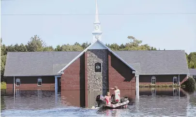  ?? AP PHOTOS ?? AFTERMATH: Marvin Singleton and Michele Larrimore, above, motor past the Pine Grove Baptist Church Saturday. Candi Cisson, below left, stands on the porch of the flooded home where she lives with her fiance, Brian Terry, on Saturday in Brittons Neck, S.C.