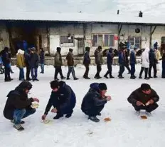  ?? AP ?? Refugees squat in the snow as they eat a warm meal distribute­d by aid groups as others queue for their portion outside a makeshift shelter in Belgrade, Serbia.