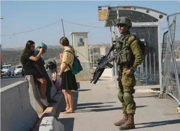  ?? MAYA ALLERUZZO/AP ?? An Israeli soldier secures a bus stop while Israeli settlers wait for a ride Thursday at the Gush Etzion transporta­tion hub for a number of West Bank Jewish settlement­s. Israeli settlers in the West Bank could soon face military rule.