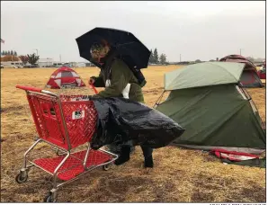  ?? AP/KATHLEEN RONAYNE ?? Amy Sheppard packs up her belongings in the rain Wednesday in a Walmart parking lot that’s been a temporary home for people displaced by wildfire in Chico, Calif. Sheppard stayed in the tent for four days with her sister and infant niece, but they were moving to a motel Wednesday to get out of the rain.