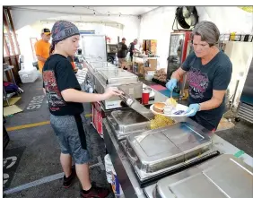  ?? NWA Democrat-Gazette/ANDY SHUPE ?? Robert Hawkins, 14, (left) and Eileen Pearce fill an order Friday in the official barbecue tent during the annual Bikes, Blues & BBQ Motorcycle Rally in Fayettevil­le. This is the first year organizers have put together an official food option at the...