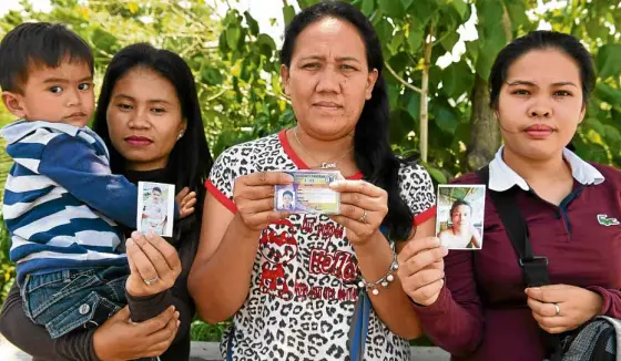  ?? —AFP ?? LOST IN SIEGE Alma Tome (left), Evelyn Powao and Melgie Powao show journalist­s photos of their husbands who remain missing a year after the Marawi siege. Another resident, Fatima Lumabao (not in photo) is looking for four of her eight children who...