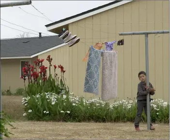  ?? PHOTO BYRHONDA LYONS FOR CALMATTERS ?? a boy stands next to a clothes line in Watsonvill­e, Calif., where migrant farmworker­s live working the fields.