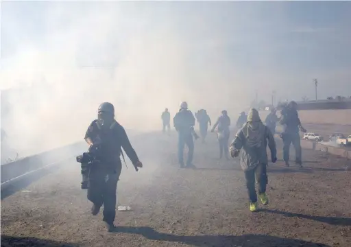  ?? RODRIGO ABD/AP ?? Migrants run from tear gas launched by U.S. agents, amid photojourn­alists covering the border, after a group got past Mexican police on Sunday at the Chaparral crossing in Tijuana, Mexico.