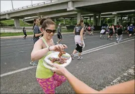  ?? AMERICAN-STATESMAN 2016 ?? Catherine Craig and Melissa Heggen cook bacon near the 4-mile marker during the 39th Austin American-Statesman Cap 10K race April 10, 2016.