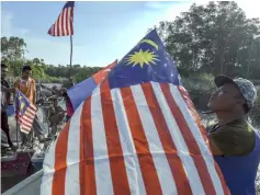  ??  ?? An Orang Asli man from Kampung Baru, Kuala Benut decorates his boat with the Jalur Gemilang. — Bernama photo