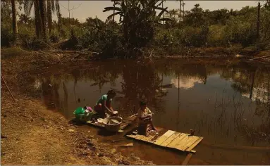  ?? Alexandre Cruz-Noronha / For The Washington Post ?? Antonia Franco dos Santos and her grandson Davi wash dishes in late July at a pond near their home in Rio Branco. By late August, after more than a month without rain, the pond had diminished to a muddy puddle.