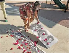  ??  ?? HARLINS KILGORE places rose petals on photos of Latasha at the playground. “I believe we’re still stereotype­d all the time,” she said.